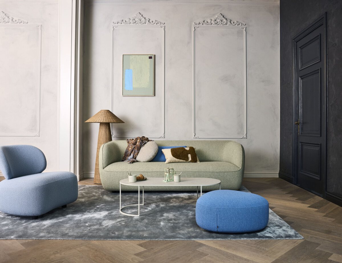 EYYE Milo bank in lichtgroene stof met afgeronde armleuningen in een stijlvol interieur met klassieke wandpanelen. EYYE Milo bank in lichtgroene stof