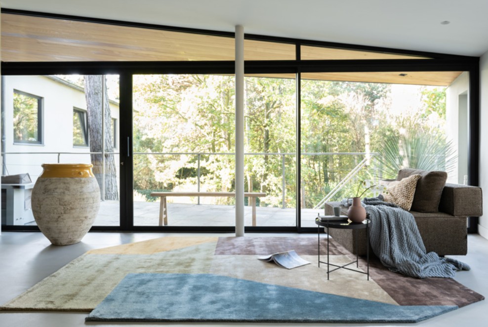 Astrada design vloerkleed met kleurrijke vlakken in modern interieur Munk Carpets handtuft Astrada karpet met geometrisch patroon in een lichte woonkamer met grote raampartijen