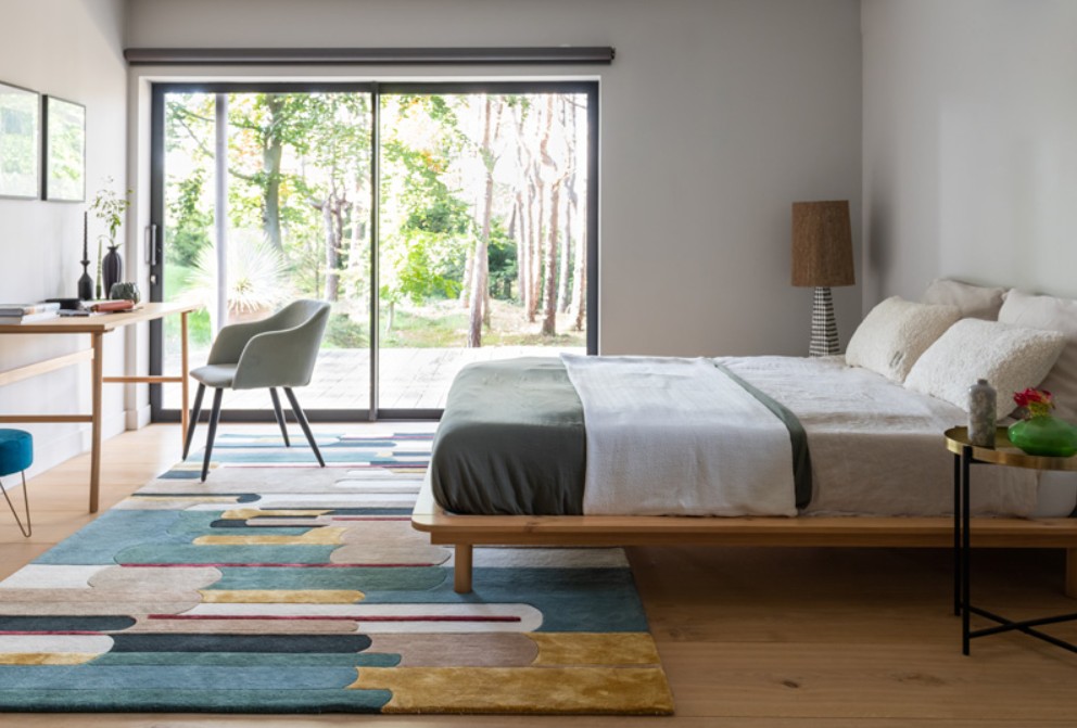 Giusti handgetuft design vloerkleed in lichte slaapkamer met natuurlijke materialen Munk Carpets Handtuft Giusti vloerkleed met kleurrijk grafisch dessin in een moderne slaapkamer met houten bed